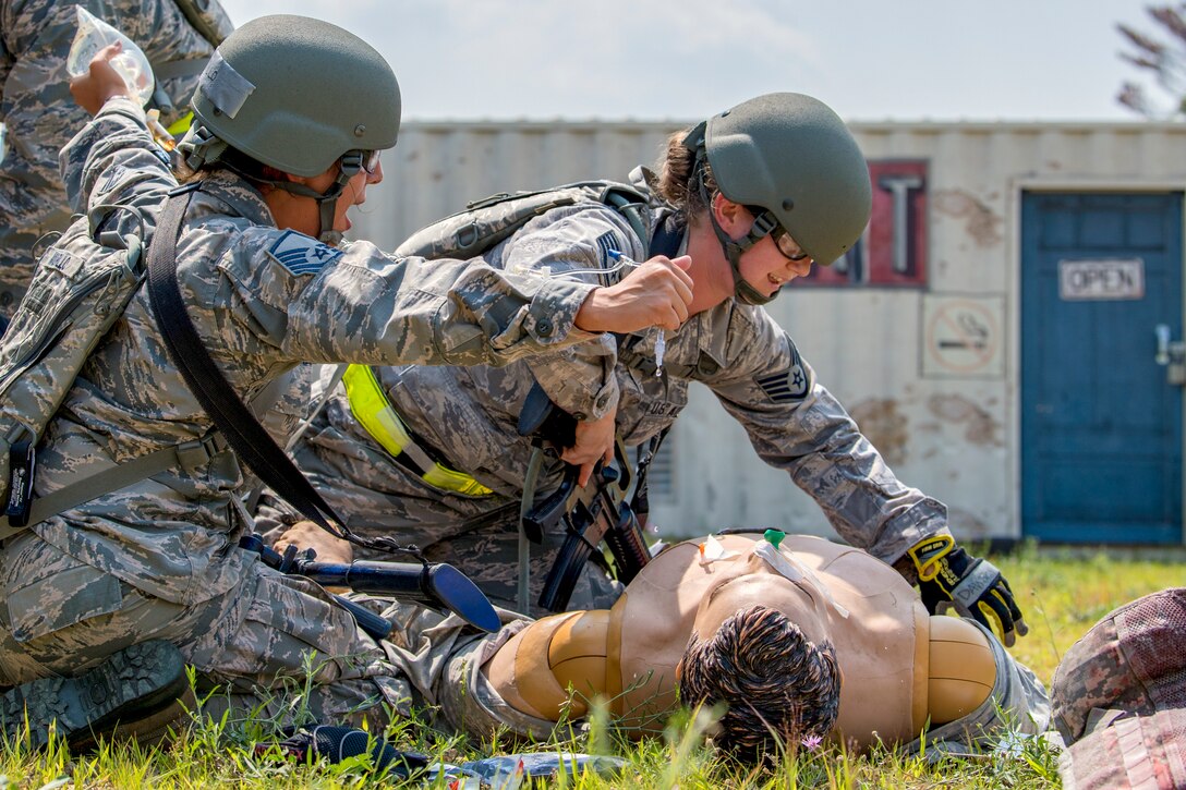 Two airmen practice putting an IV into a practice dummy.