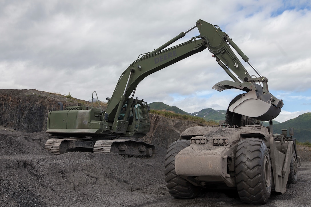 Sgt. Eric Jerabek, a heavy equipment operator with Headquarters Battery, 14th Marine Regiment, 4th Marine Division unloads gravel from an excavator into a wheel tractor-scraper to be laid onto the runway during Innovative Readiness Training, Old Harbor, Alaska, Aug. 5, 2018. This year marks the completion of the 2,000-foot extension of Old Harbor’s runway. (U.S. Marine Corps photo by Lance Cpl. Tessa D. Watts)