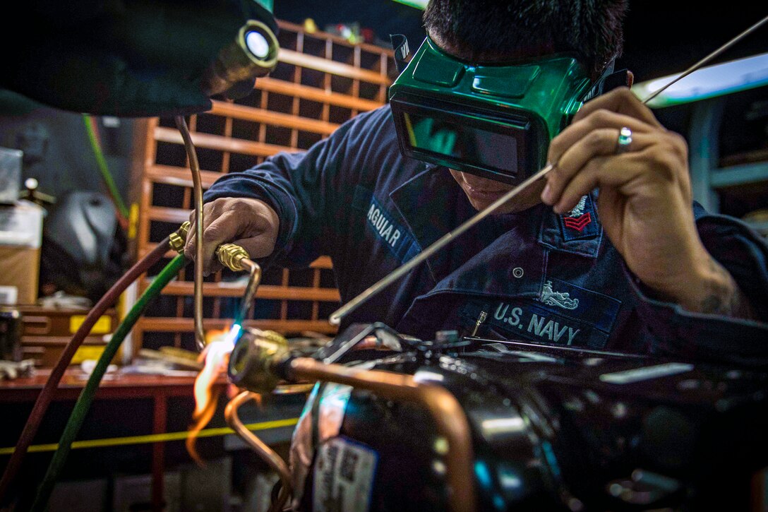 A sailor uses a welding torch on metal piping.