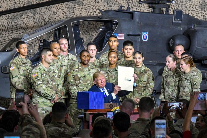 President Donald J.Trump poses with service members in front of a helicopter.