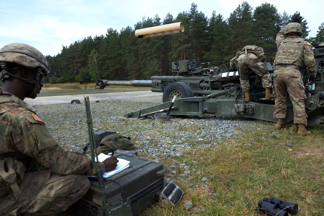 A soldier tosses an empty shell casing, while a team member writes down notes after firing an M777A2 howitzer.