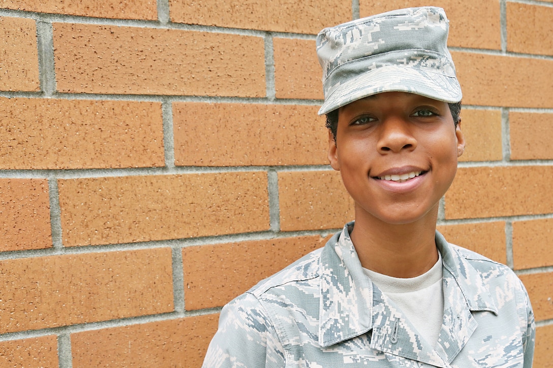 An airman poses for a photo in front of a red brick wall.