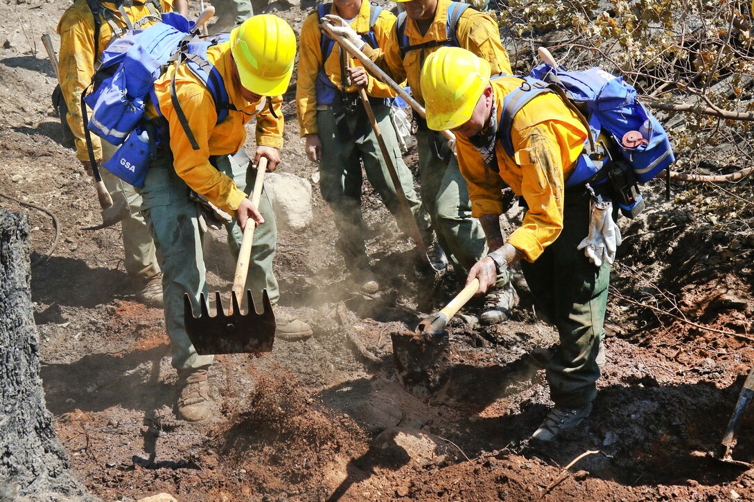 Oregon Army National Guardsmen and firefighters use shovels and rakes to fight a wildfire.