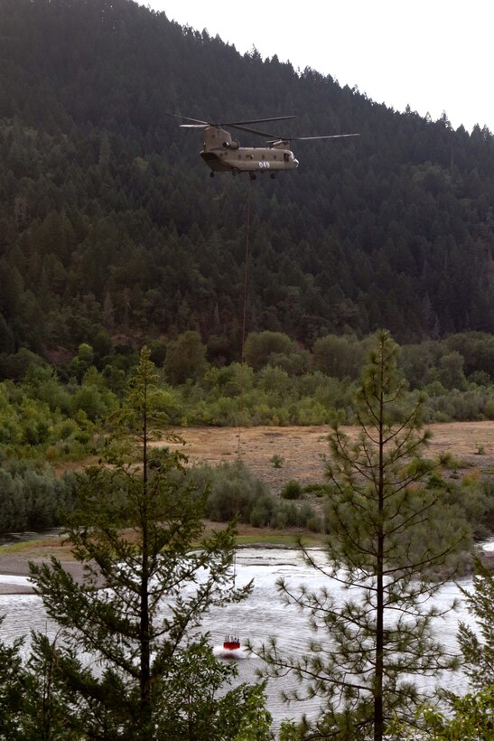 A CH-47 Chinook helicopter crew refills a bucket firefighting system with water.