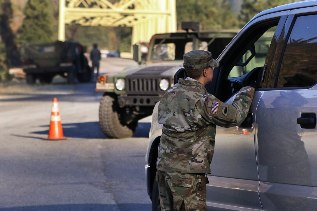 A soldier speaks with a firefighter at a traffic assistance control point.