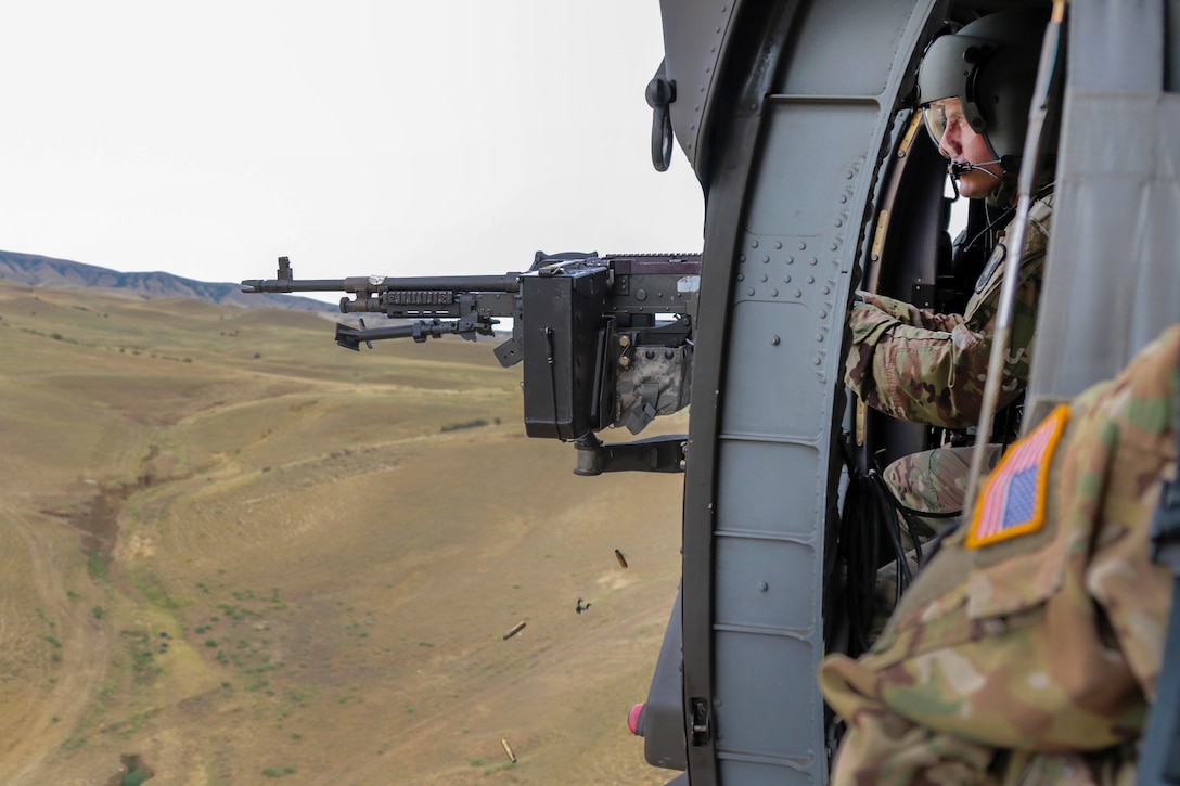 A soldier fires an M240B machine gun from an UH-60 Black Hawk helicopter.