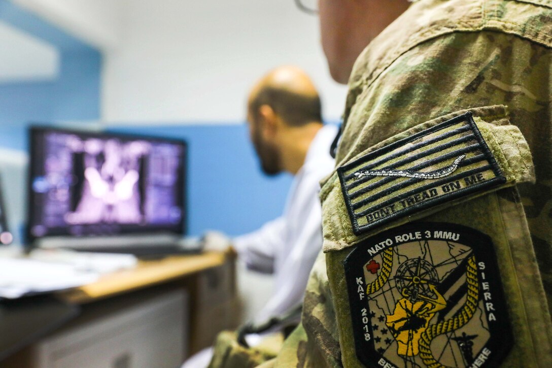 An American radiology technician observes as an Afghan radiology technician checks the results of an X-ray.