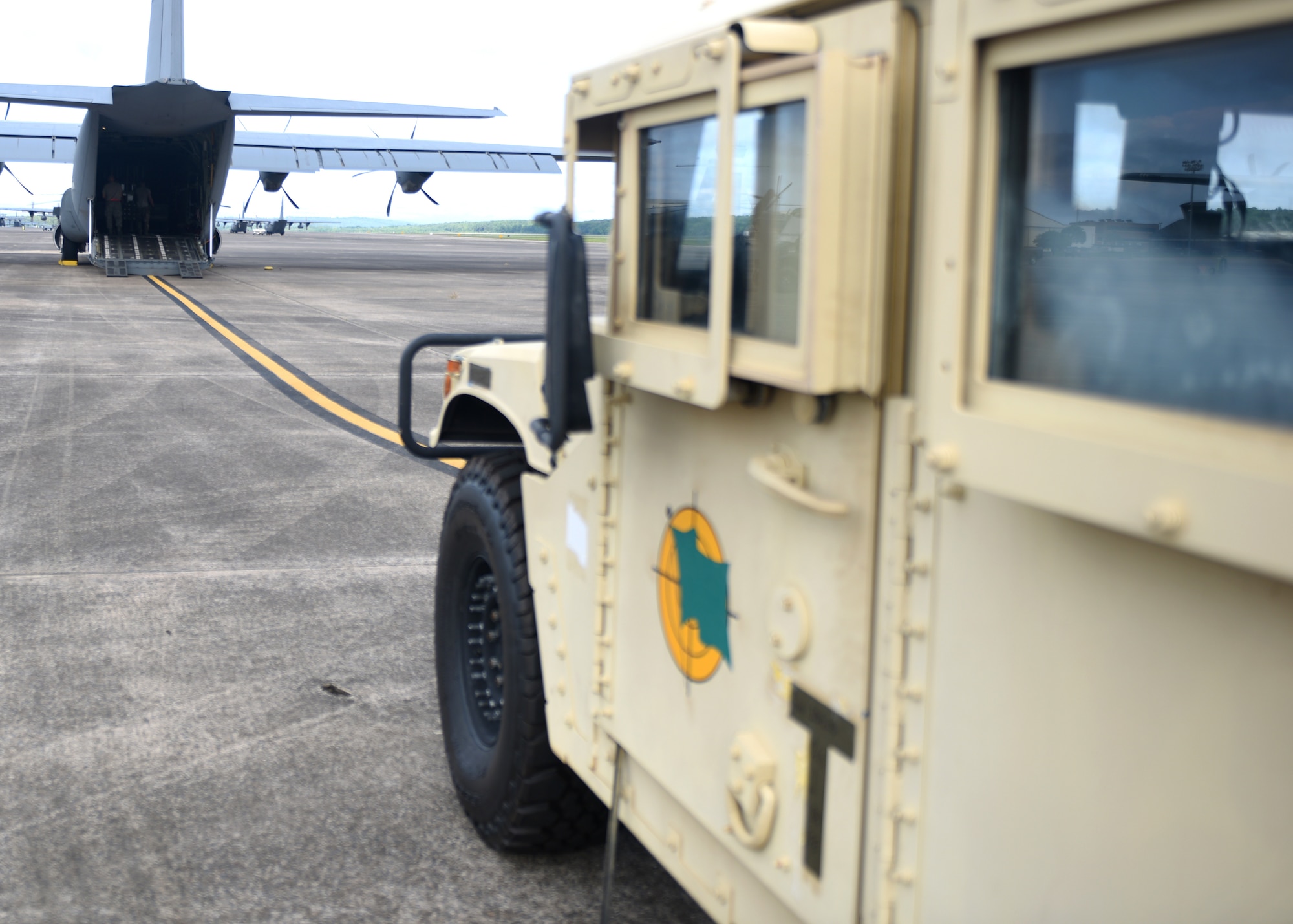 A male in uniform loads a grey C-130J with a vehicle.