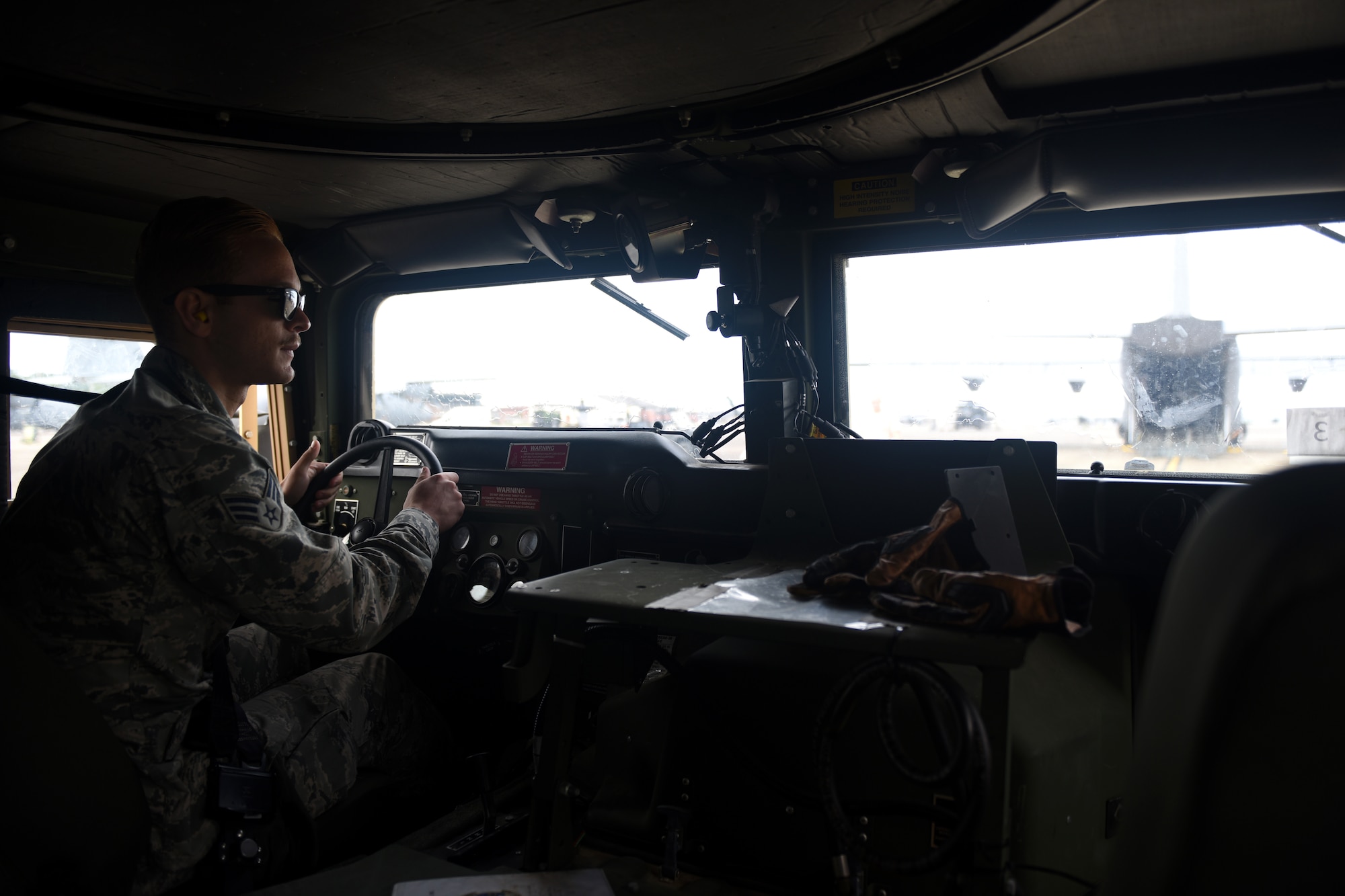 A male in uniform loads a grey C-130J with a vehicle.