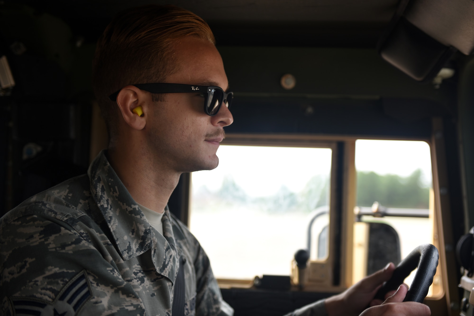 A male in uniform loads a grey C-130J with a vehicle.