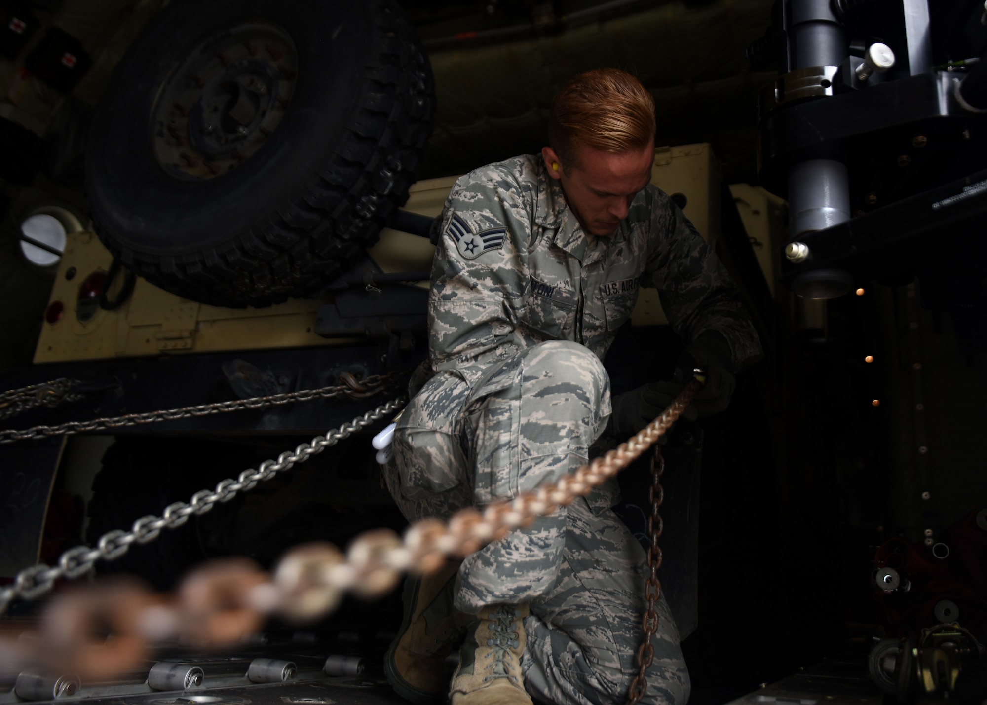 A male in uniform loads a grey C-130J with a vehicle.