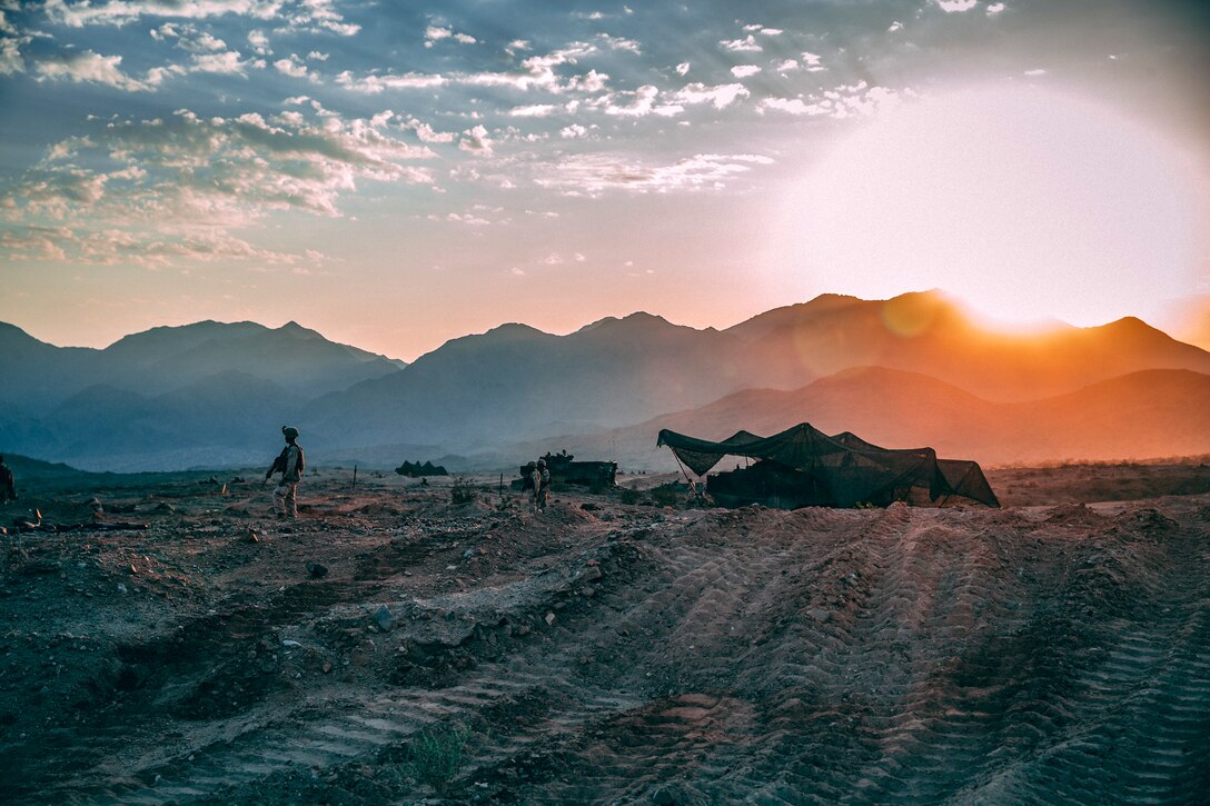 A Marine stands watch outside of a campsite as night falls.