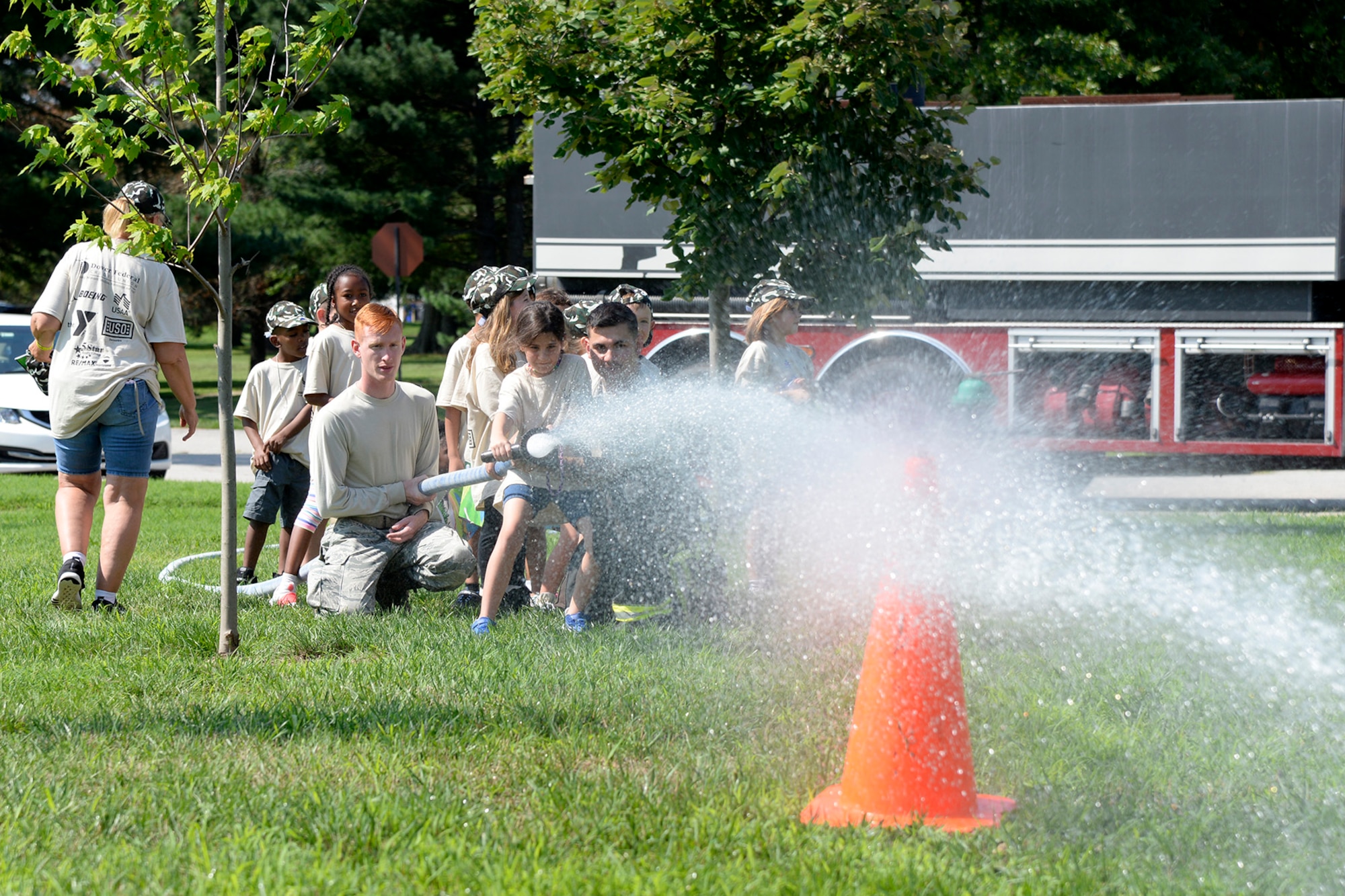 Firefighters from the 436th Civil Engineer Squadron let children operate a fire hose during a Kids/Teachers Understanding Deployment Operations event Aug. 9, 2018, at Dover Air Force Base, Del. Children and teachers learned about different support functions on base and how they contribute to the rapid global mobility mission. (U.S. Air Force photo by Tech. Sgt. Matt Davis)