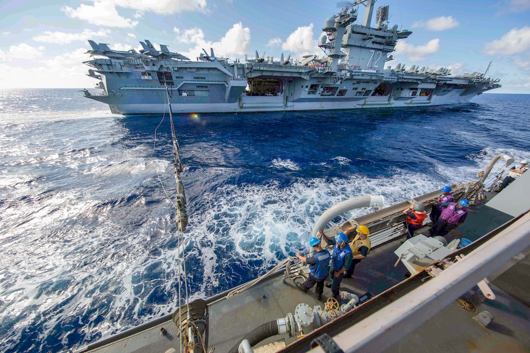 Two ships at sea attach to each other with long ropes.