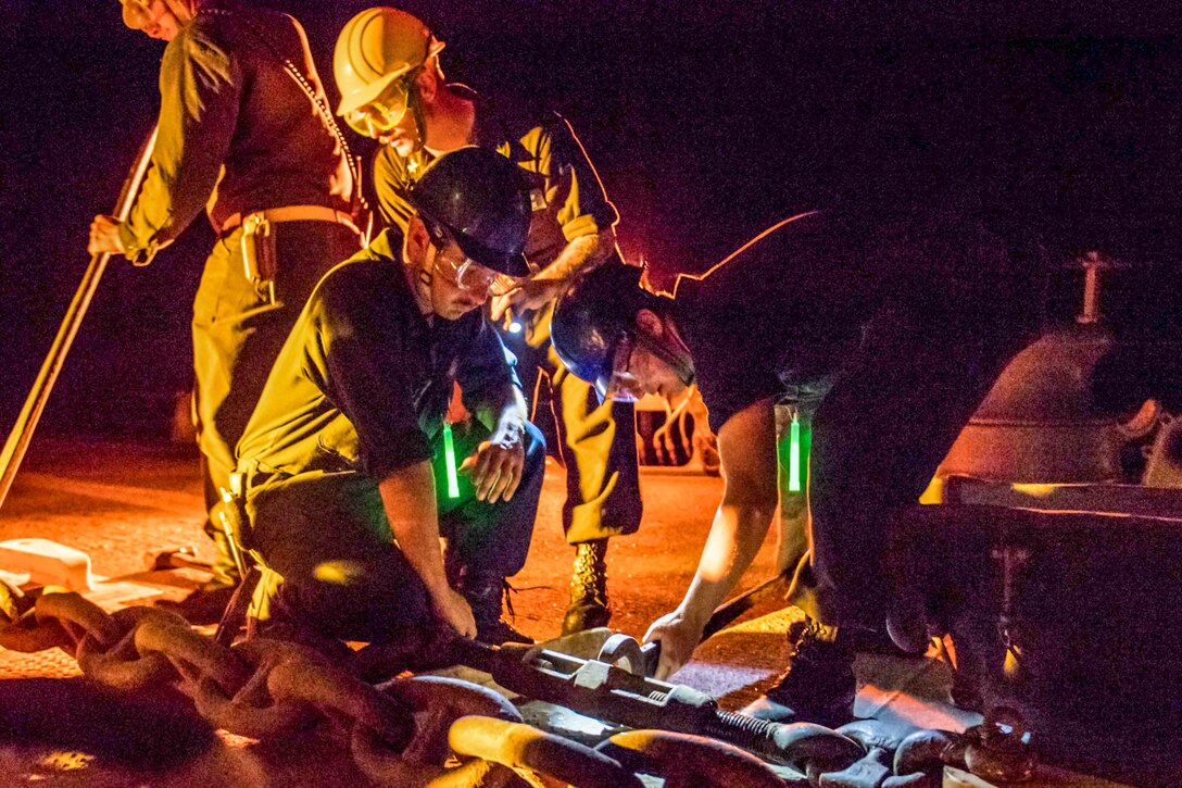 Sailors tighten equipment on a naval vessel.