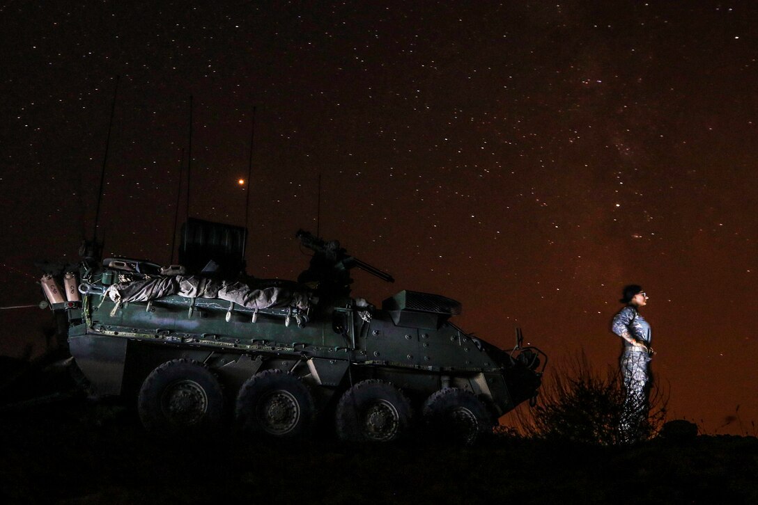 A guardsman stands in front of her vehicle and looks at the night sky.