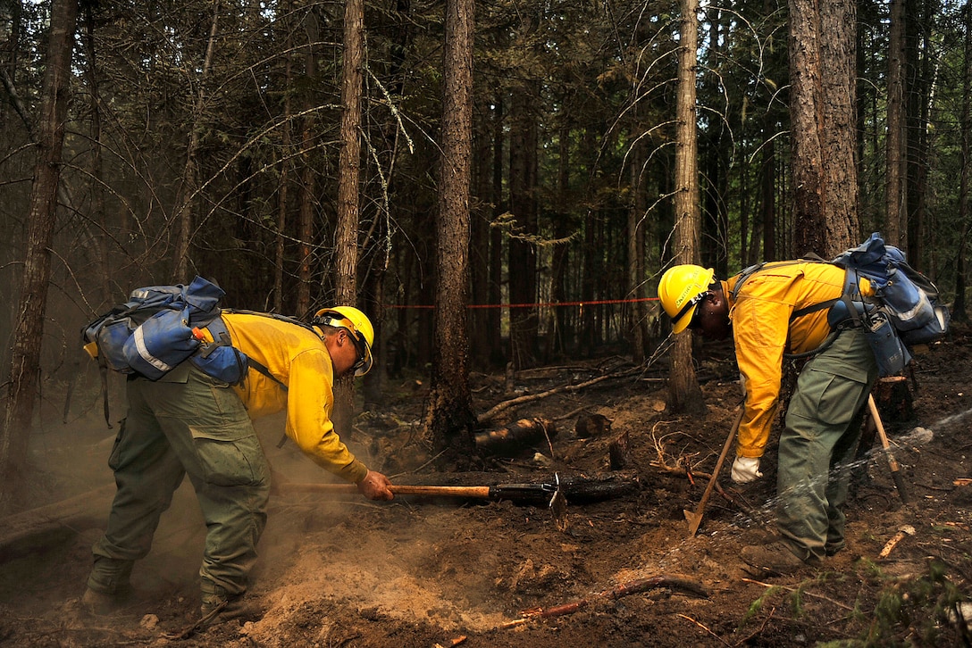 Soldiers and airmen use shovels to clear hot spots along a fire line.