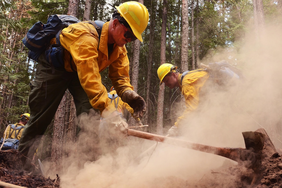 A soldier uses a pickaxe to clear hot spots along a fire line.