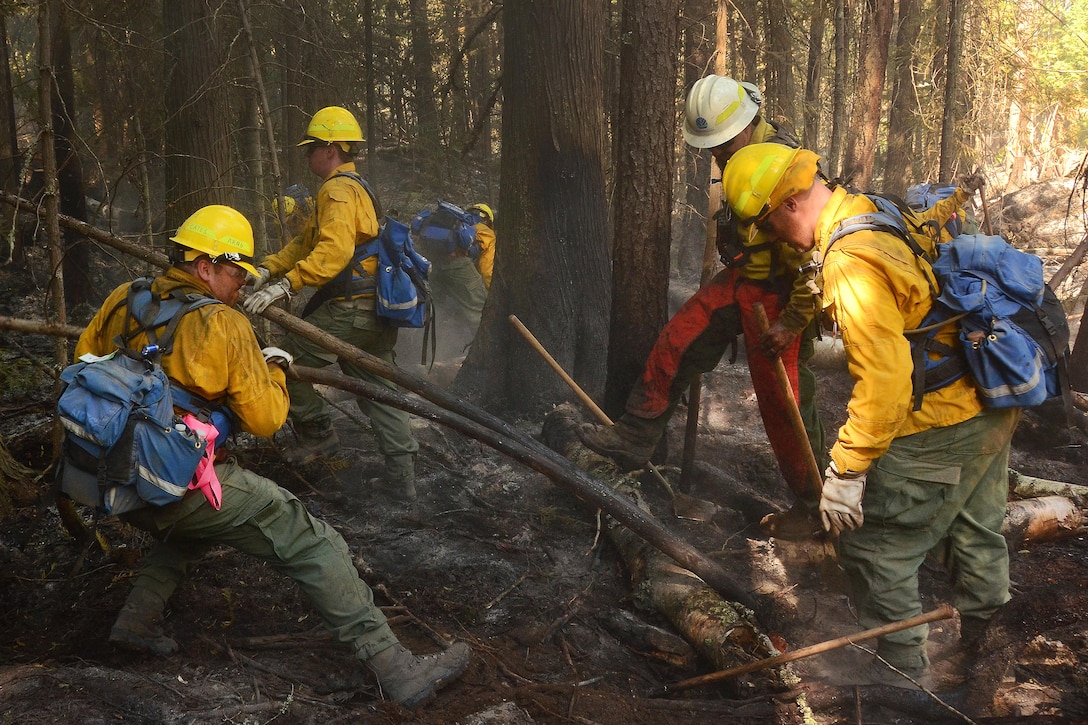 Airmen clear burnt wood and debris from a fire line.