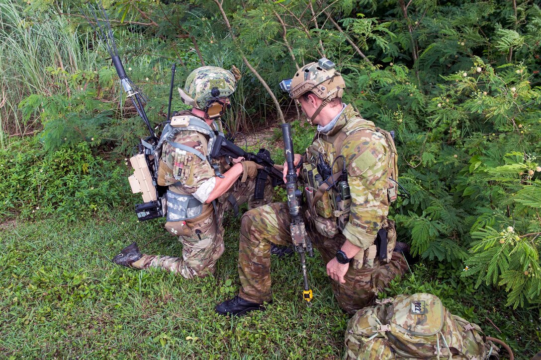 A U.S. sailor and Australian soldier kneel at a trailhead.