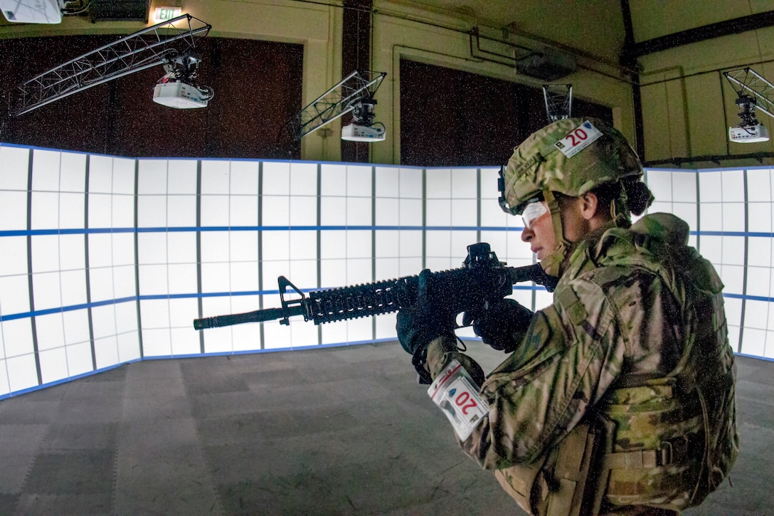 A soldier aims her weapon inside in front of a wall of lights.