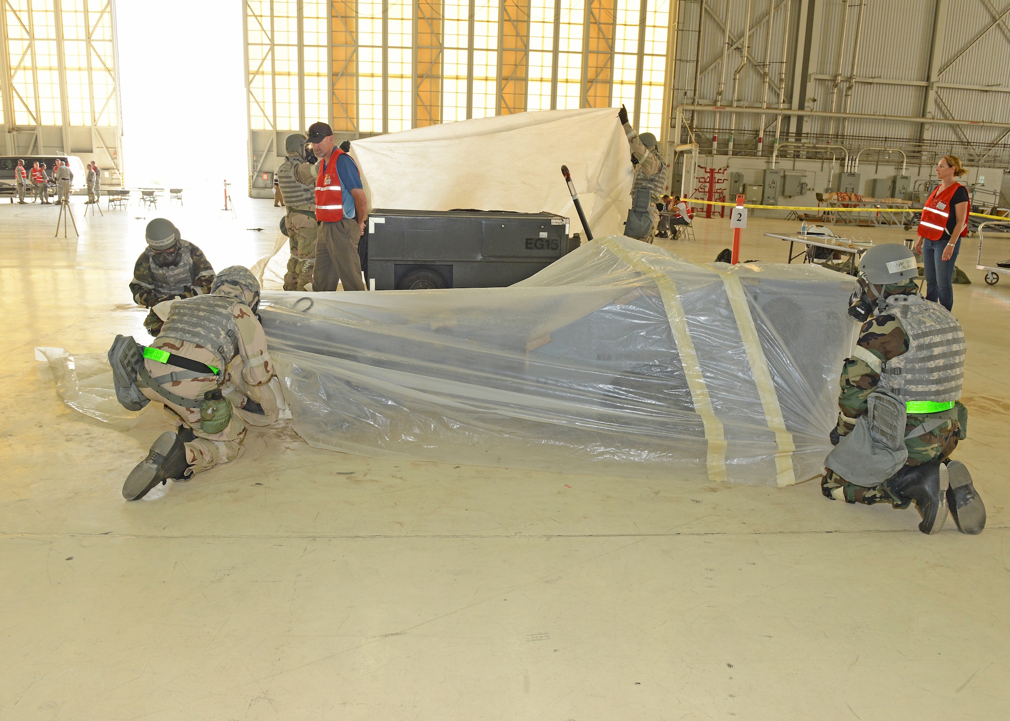 Airmen wearing their mission oriented protective posture, or MOPP gear, wrap plastic over a jammer weapons loader to simulate protecting the equipment from chemical, biological and nuclear elements. This was one station in Hangar 1600 part of Test Wing Readiness Exercise 18-03, Aug. 9. (U.S. Air Force photo by Kenji Thuloweit)