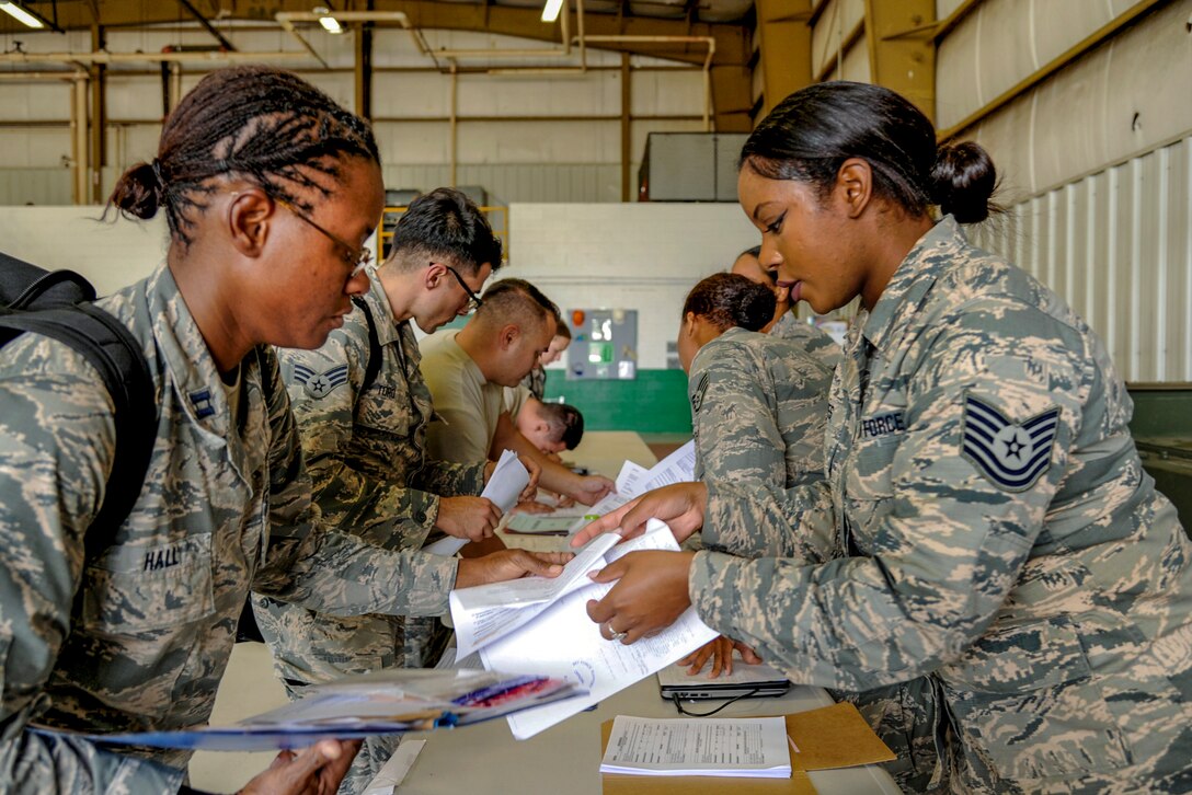 An airman checks in another airman at a table.