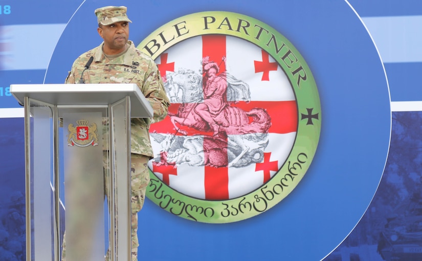 An Army officer speaks at a podium in front of a large red and white logo.