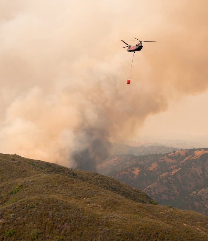 Helicopter approaches to drop water on a wildfire.