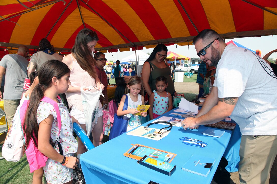 Chris Zamets of Brightwood College in Palm Springs hands out school supplies and information during the Back to School Bash at Victory Field, Marine Corps Air Ground Combat Center, Twentynine Palms, Calif., Aug. 10, 2018. About 1,500 attended the event hosted by Marine Corps Community Services and the Combat Center School Liaison. (Marine Corps photo by Kelly O'Sullivan)