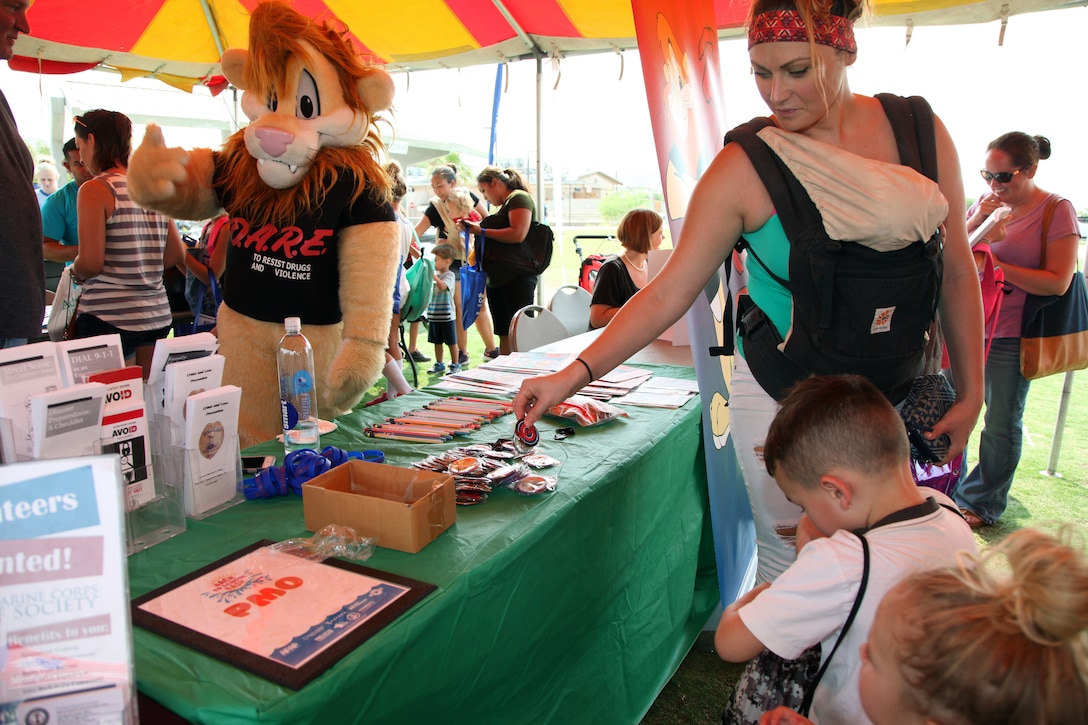 Daren the DARE Lion looks on while family members peruse items at the Provost Marshal's Office booth during the Back to School Bash at Victory Field, Marine Corps Air Ground Combat Center, Twentynine Palms, Calif., Aug. 10, 2018. About 1,500 attended the event hosted by Marine Corps Community Services and the Combat Center School Liaison. (Marine Corps photo by Kelly O'Sullivan)