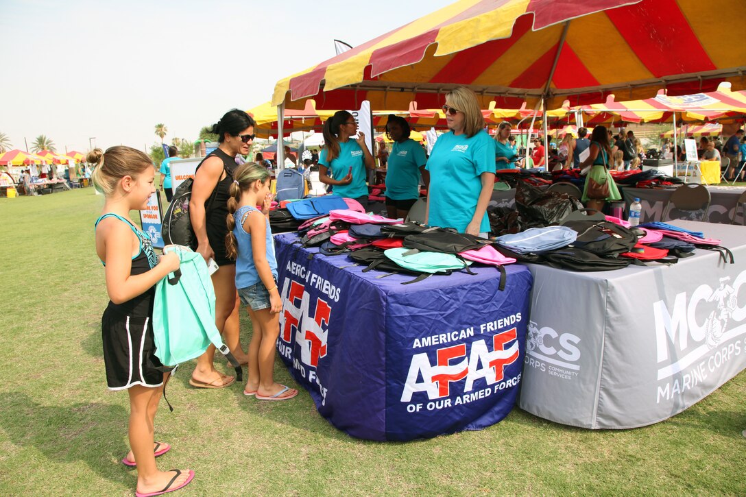 Kathryn Crank, right, Marine Corps Community Services Marketing Director, encourages young students to take a free backpack during the Back to School Bash at Victory Field, Marine Corps Air Ground Combat Center, Twentynine Palms, Calif., Aug. 10, 2018. About 1,500 attended the event sponsored by MCCS and the Combat Center School Liaison Office. (Marine Corps photo by Kelly O'Sullivan)