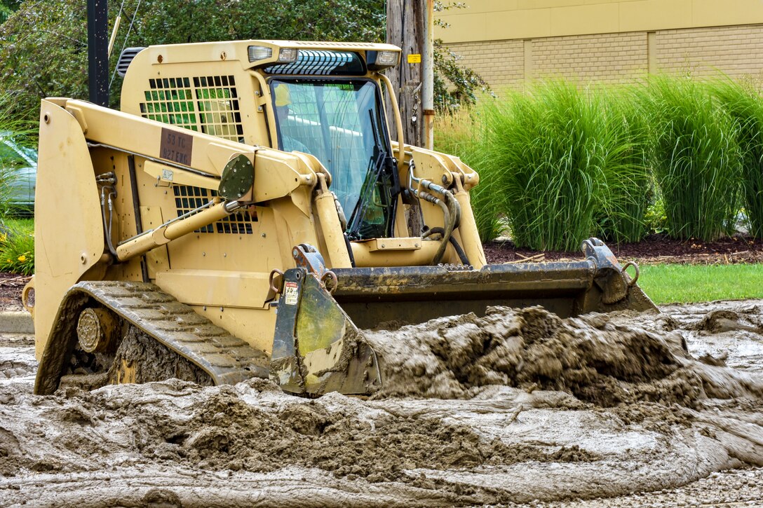 A soldier pushes through mud in a construction vehicle.