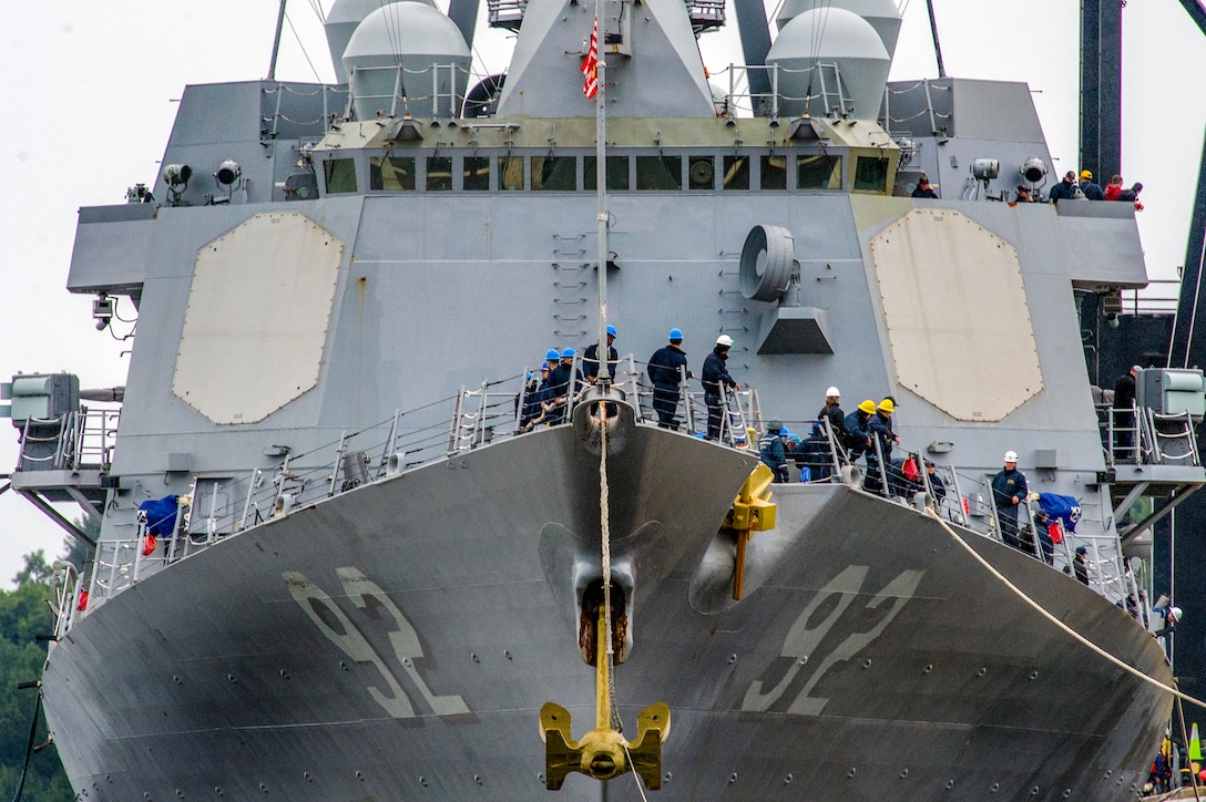 Sailors communicate around the bow of a large ship.