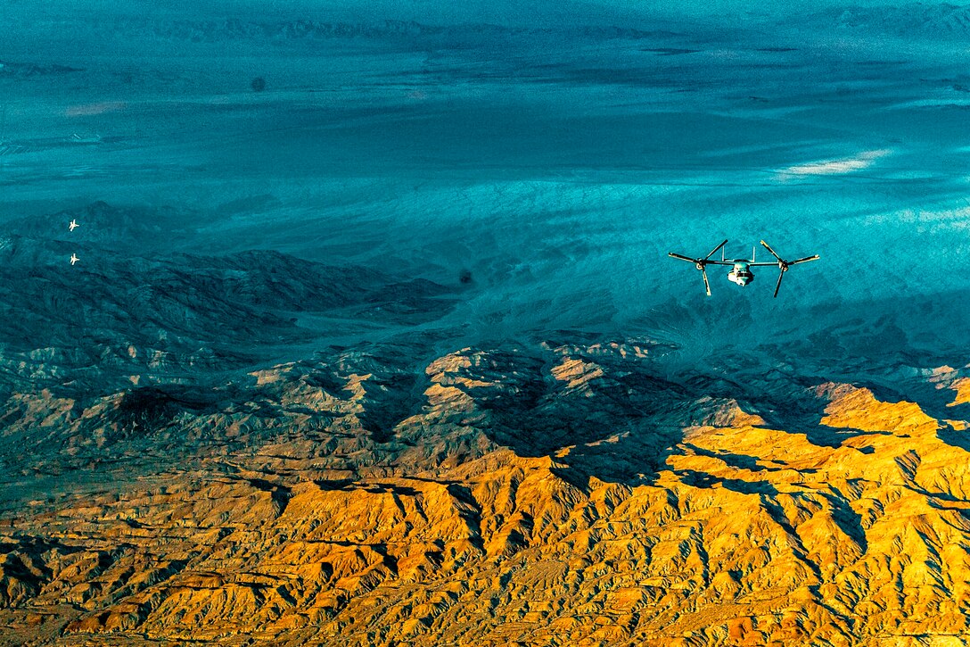 Seen from above, two Hornets and an Osprey fly over the desert.