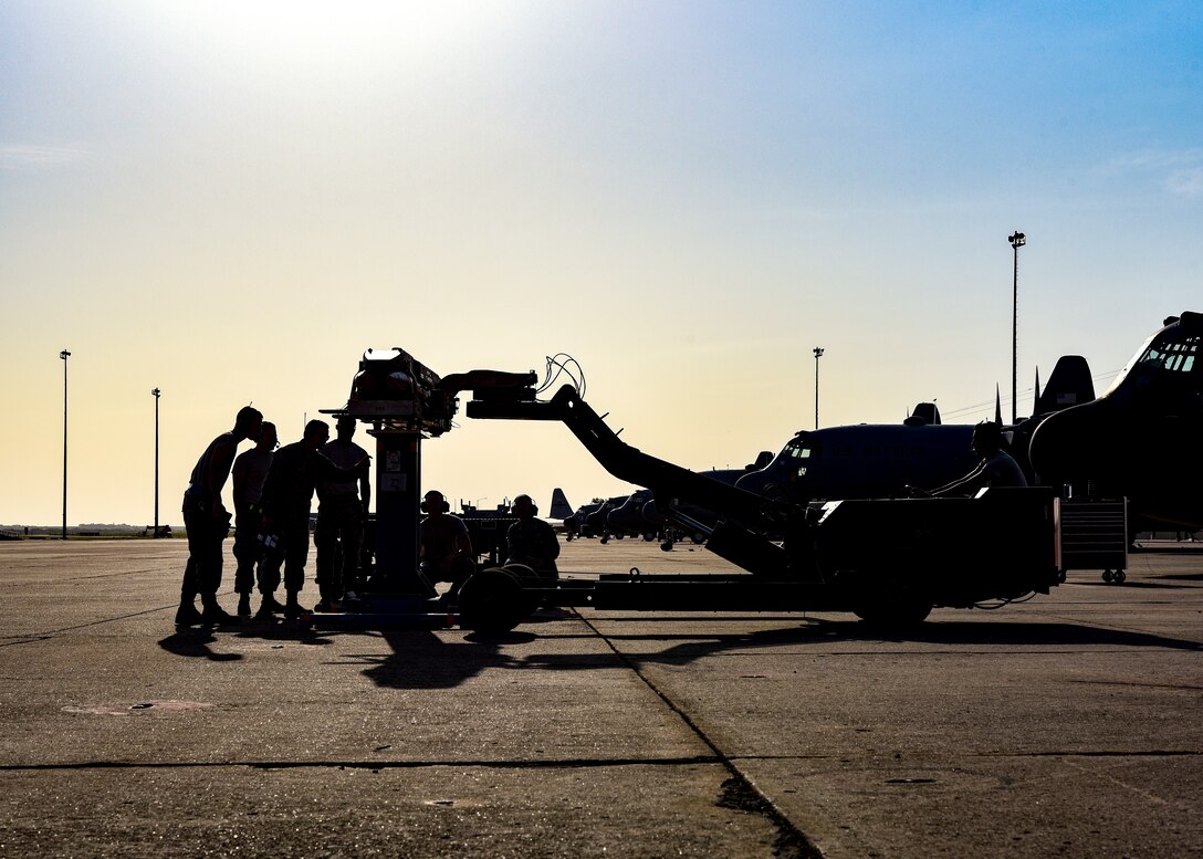 An instructor points to a specific spot where the bomb rack will connect to the cradle. The sun silhouettes them.
