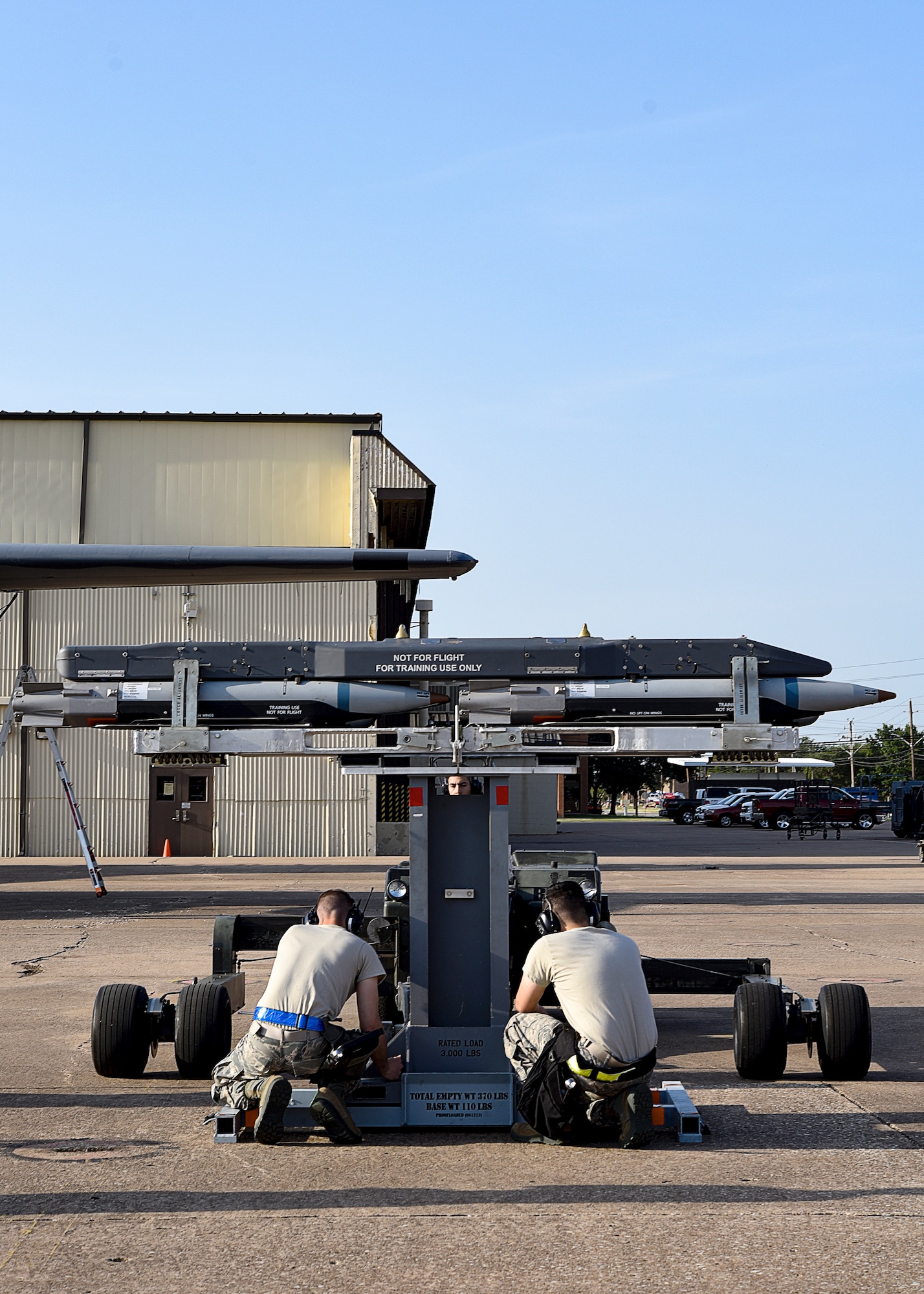 Airmen secure a bomb cradle to a bomb loader as they prepare to load bombs.