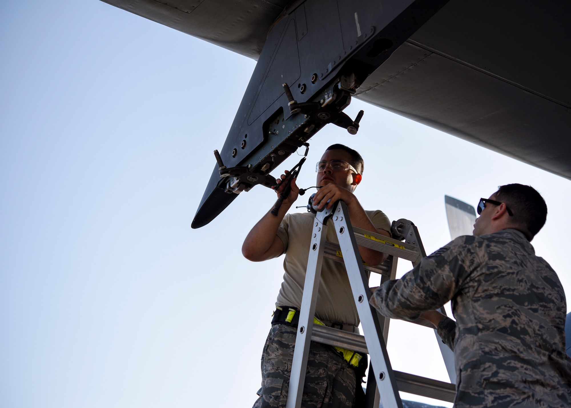 An Airman cuts wires on a bomb rack to set it up for a different kind of bomb.