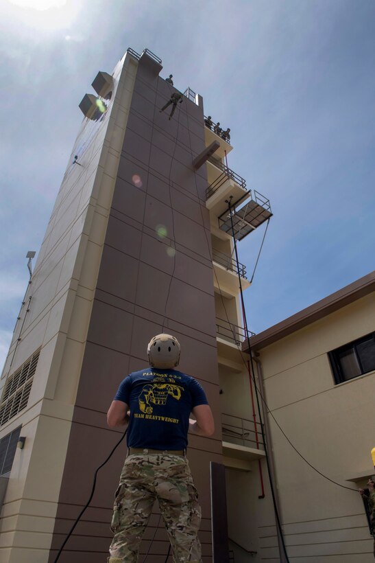 A U.S. sailor, foreground watches as an Australian soldier repels from a tower during unit-level training.