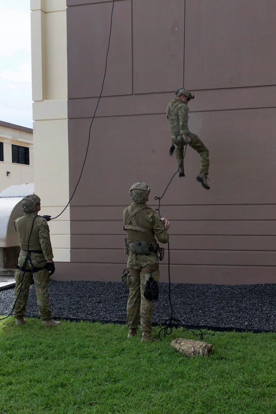 Australian soldiers watch as a team member repels from a tower during unit-level training.