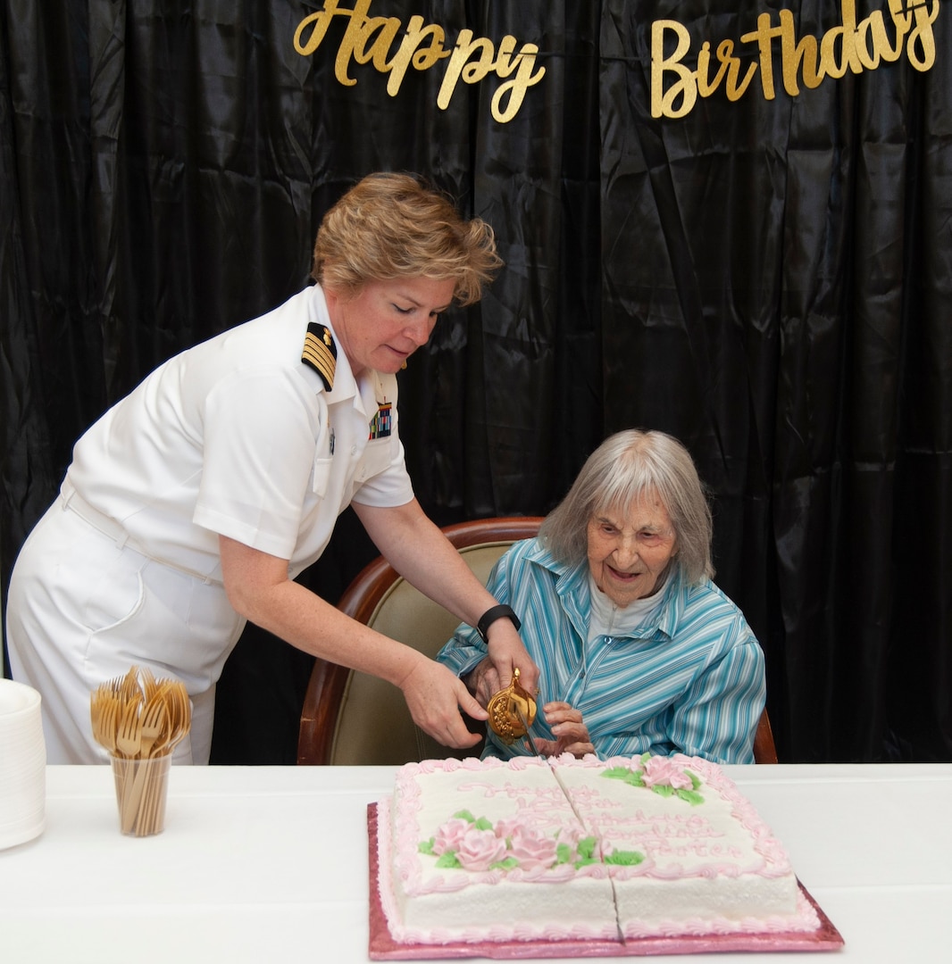 Capt. Maryann Mattonen (left), Navy Medicine Training Support Center commanding officer, and Blondina Porter cut Porter's  birthday cake together with a Navy officer ceremonial sword at the San Antonio Brookdale Assisted Living Facility to wish the World War II Navy Nurse a happy 100th birthday Aug. 15.