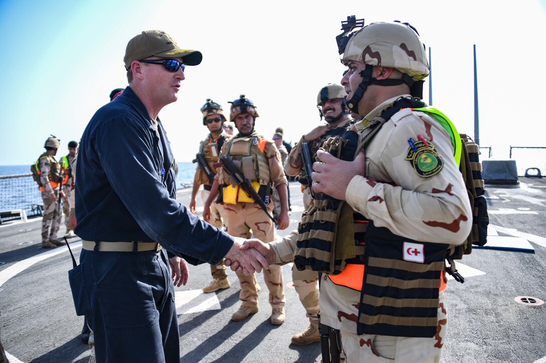 180814-N-RM440-2548 ARABIAN GULF (August 14, 2018) Cmdr. Russ Moore, guided-missile destroyer USS The Sullivans (DDG 68) commanding officer, left, shakes hands with a member of the Iraqi visit, board, search and seizure team during a trilateral exercise with Iraq and Kuwait. The exercise is a surface engagement between the U.S. Navy and Coast Guard and the Iraqi and Kuwaiti navies focused on improving proficiency in maritime security tactics to help ensure the freedom of navigation throughout the U.S. 5th Fleet area of operations (U.S. Navy photo by Mass Communication Specialist 2nd Class Samantha P. Montenegro/Released)