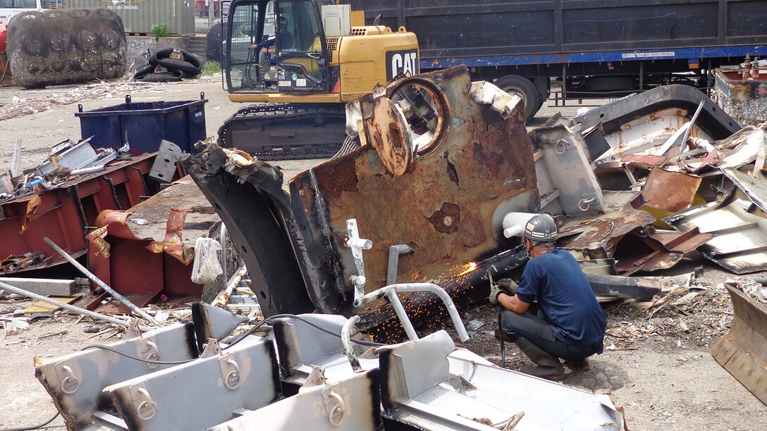 A scrap contractor employee uses a torch to cut pieces of a large work boat even smaller.