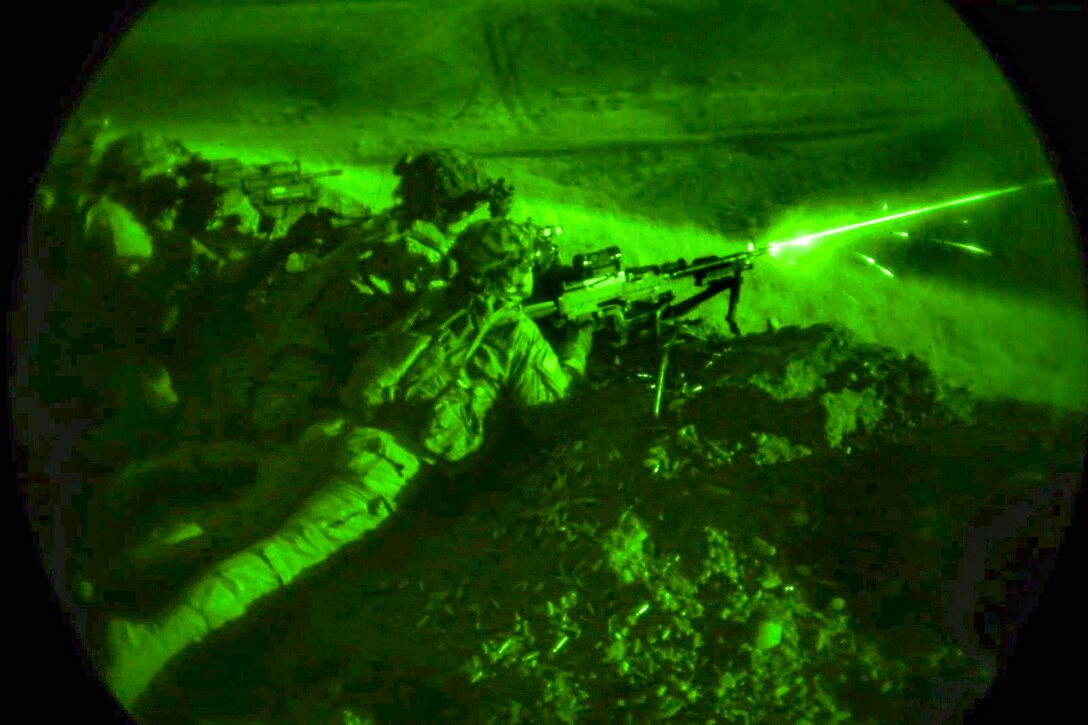 A soldier fires a weapon from a prone position at night.