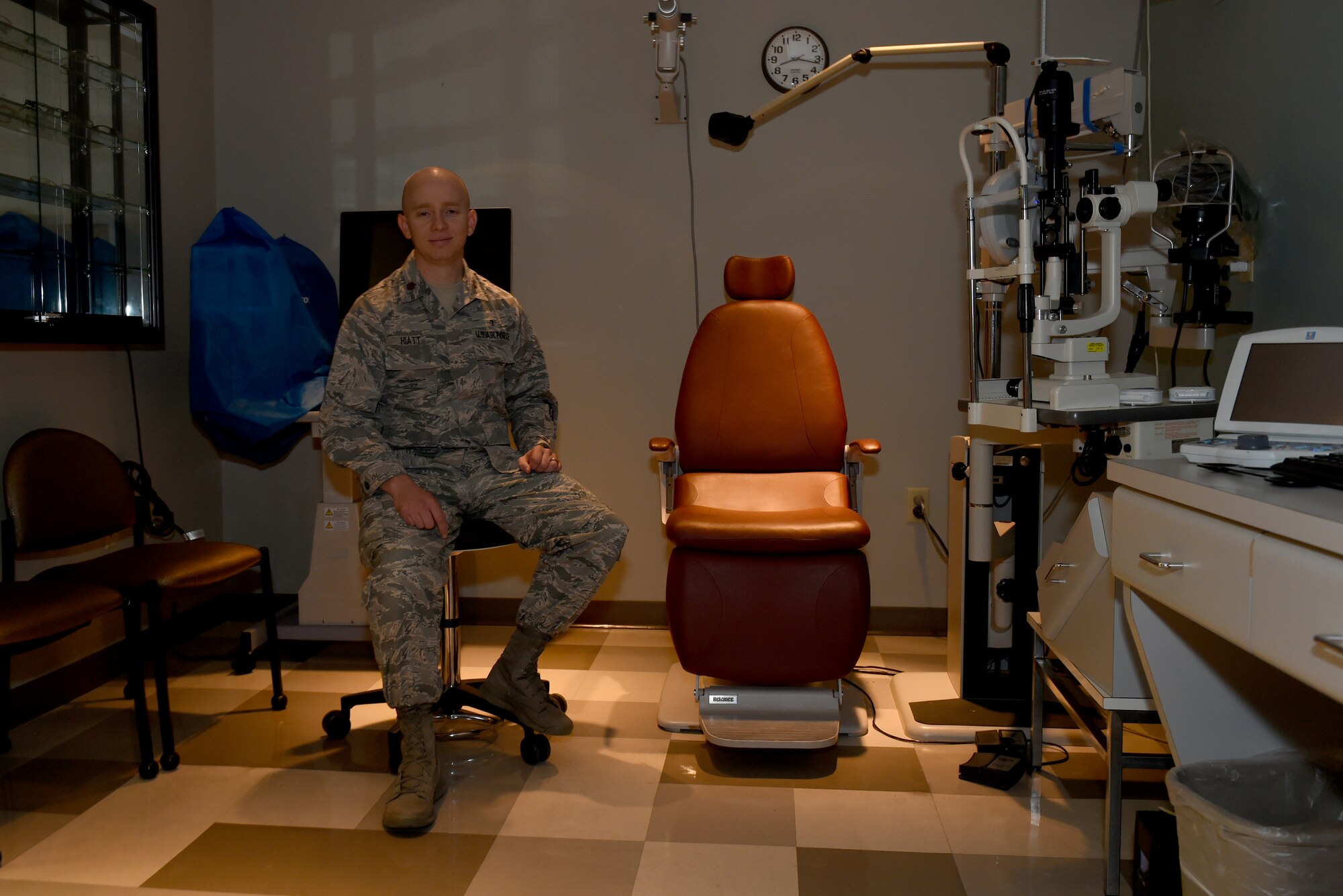 Photo of Maj. Hiatt sitting next to empty patient chair where eye exams are administered.