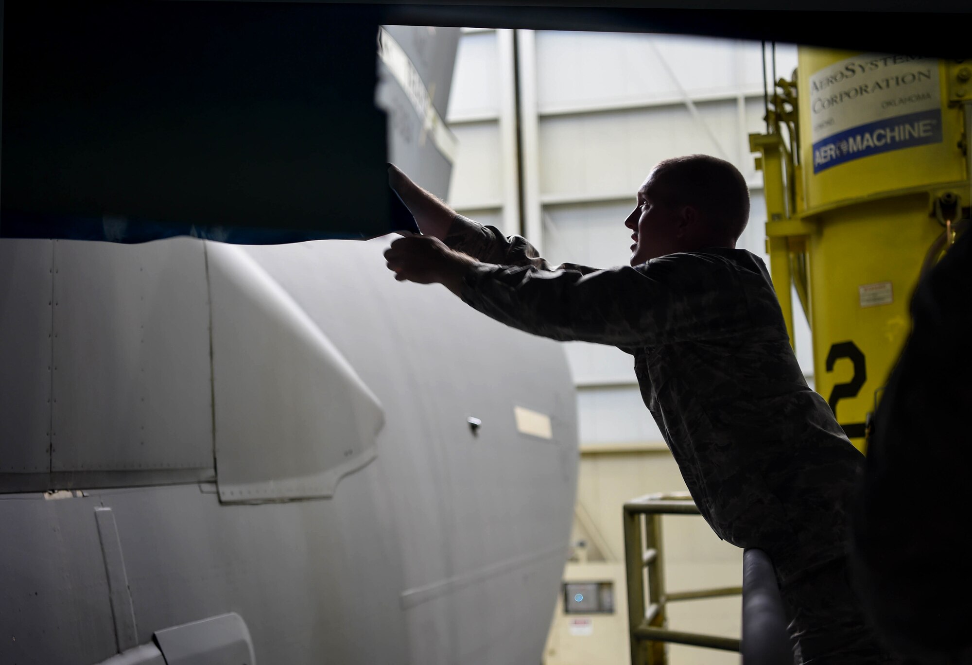 Staff Sgt. Cody Lange, 60th Maintenance Squadron aircraft structural maintenance technician, removes plastic covering a section of a C-17 Globemaster III from Travis Air Force Base, Calif., which was placed there to protect it while the C-17 was painted Aug. 6, 2018, at Joint Base Lewis-McChord, Wash. California laws prevent Travis Airmen from spray painting their C-17s, so they brought it to McChord where it is allowed. (U.S. Air Force photo by Senior Airman Tryphena Mayhugh)