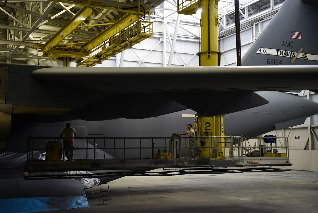 Tech. Sgt. Salvador Ynostraza, left, and Staff Sgt. Adrian Catalan, both 60th Maintenance Squadron aircraft structural maintenance technicians, maneuver a platform under the wing of a C-17 Globemaster III from Travis Air Force Base, Calif., Aug. 6, 2018, at Joint Base Lewis-McChord, Wash. Ynostraza and Catalan were part of a Travis crew sent to McChord to spray paint their C-17 in McChord’s paint barn. (U.S. Air Force photo by Senior Airman Tryphena Mayhugh)