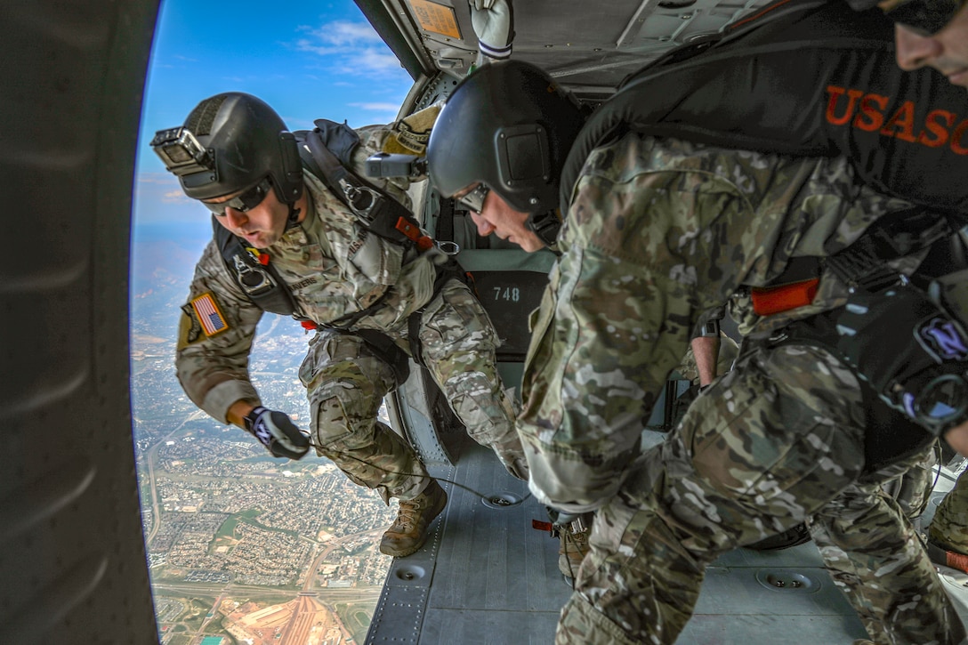Two soldiers prepare to jump from an open helicopter.