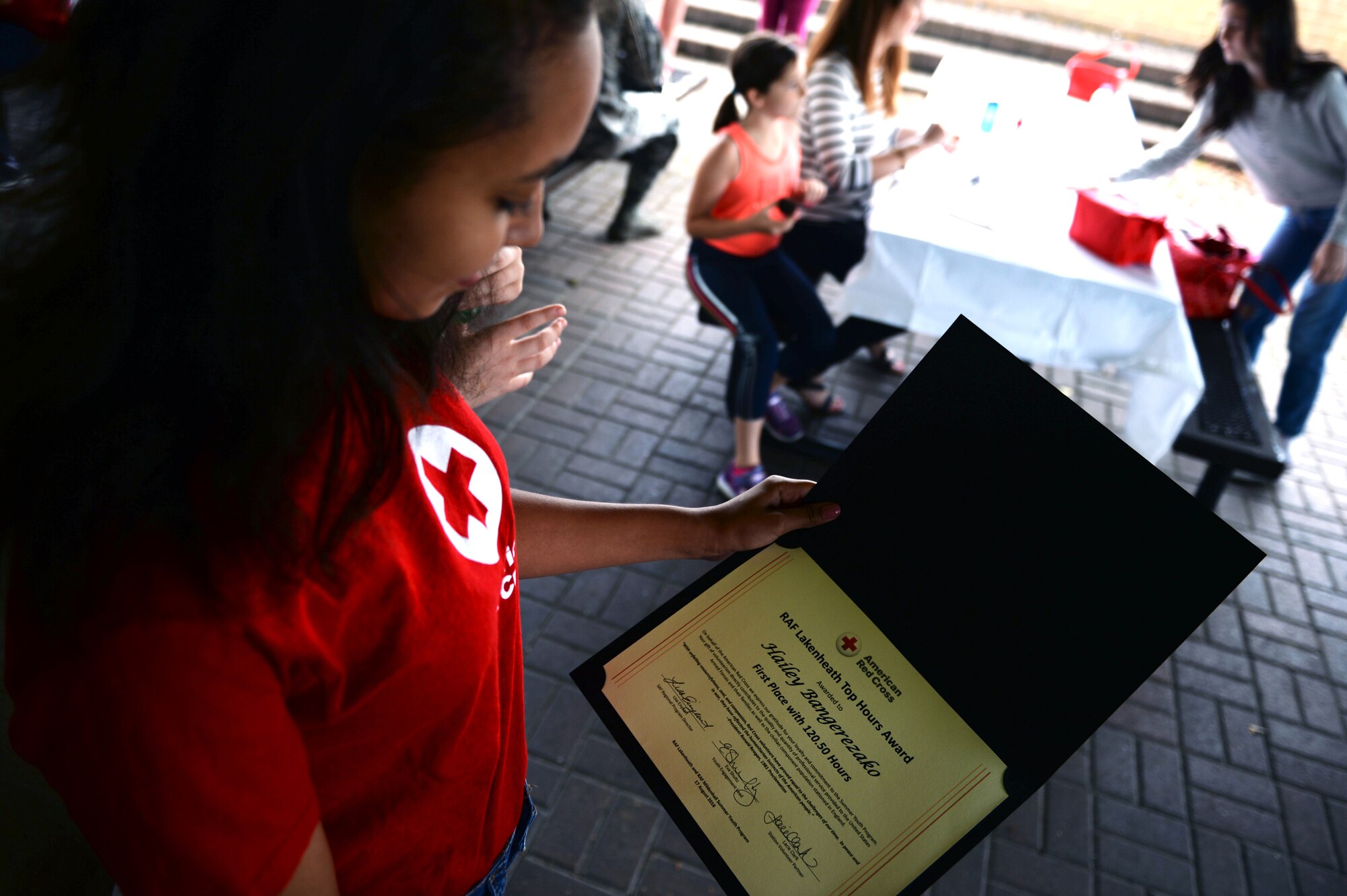 Hailey Bangerezako, a Red Cross volunteer, reads her award at the Summer Youth Program’s end of summer barbeque, Royal Air Force Lakenheath, England, Aug. 17, 2018. Bangerezako volunteered over 120 hours interning at the 48th Public Affairs Office. (U.S. Air Force photo/Airman 1st Class Shanice Williams-Jones)