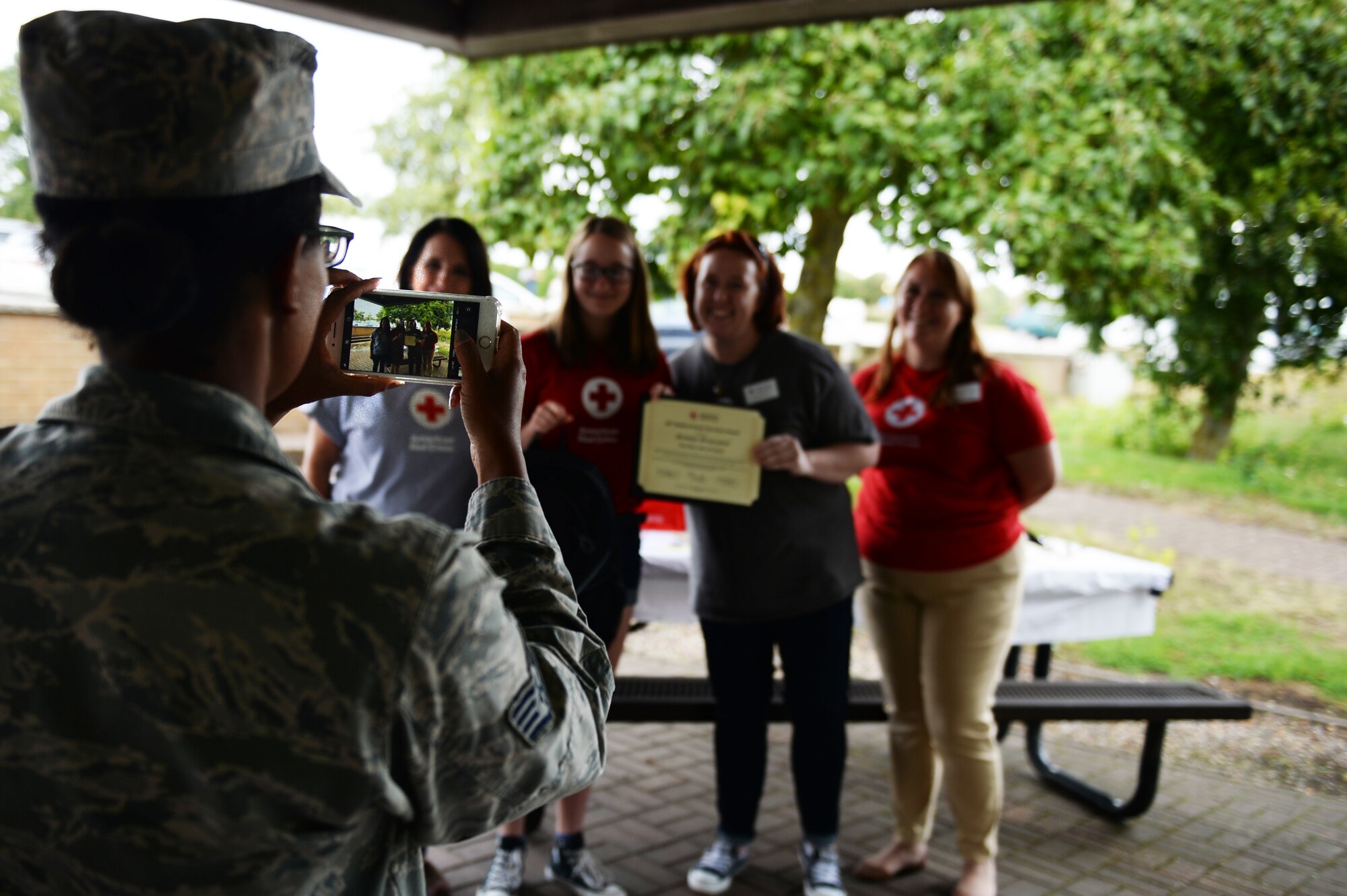 A representative of the 48th Medical Group takes a photo of a Red Cross volunteer receiving an award at the Summer Youth Program’s end of summer barbeque, Royal Air Force Lakenheath, England, Aug. 17, 2018. Summer Youth Program volunteers served at numerous locations on RAF Lakenheath, RAF Feltwell and RAF Mildenhall including the surgical department of the 48th MDG. (U.S. Air Force photo/Airman 1st Class Shanice Williams-Jones)